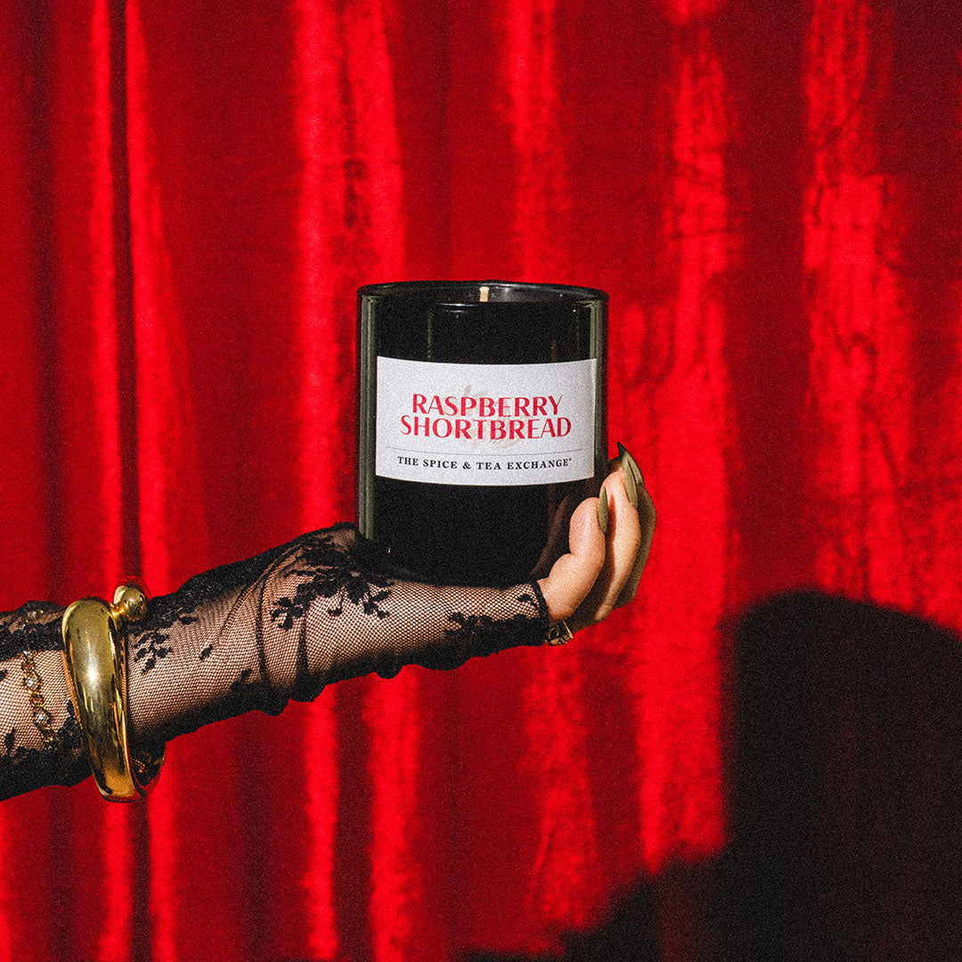 Hand holding a raspberry shortbread candle against a red curtain background